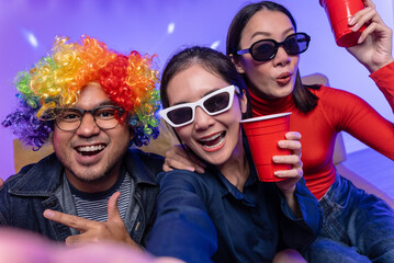 Happy asian diverse group friends taking selfie with neon light on a party using smartphone. Home party friends  having fun enjoying time and dancing together. New Year's Eve Party concept