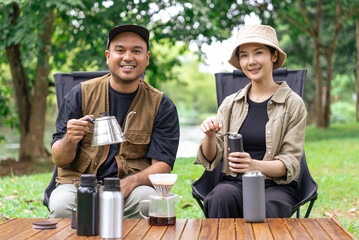 Happy asian couple making drip coffee together at camp side and looking at camera, They feeling relaxed and refreshing while camping in the nature. Recreation and journey outdoor activity lifestyle.