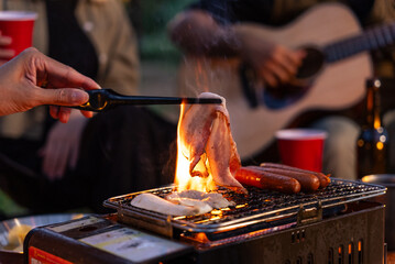 Close up of male hands grilling meat with friends camping background. They feeling exited while...