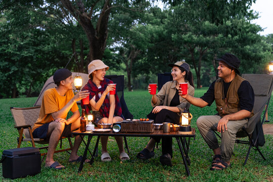 Happy asian diverse group friends enjoy drinking a beer together. They feeling relaxed and refreshing while camping in the nature at night. Recreation and journey outdoor activity lifestyle. - Powered by Adobe