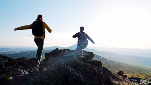 Two young traveler achieve cliff summit and enjoy scenic landscape view standing on high top of mountain above hilly valley. Tourist success on peak together outdoors
