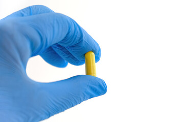 A female hand in a blue medical glove holds a yellow capsule with medicine, isolate on a white background.