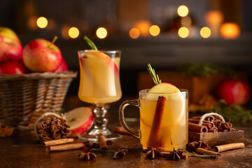 Mulled cider with apples, cinnamon, rosemary, and anise on a background of burning candles.