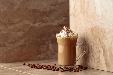 Glass cup of coffee latte on a beige ceramic table.