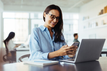 Happy business woman using a mobile phone while sitting in an office
