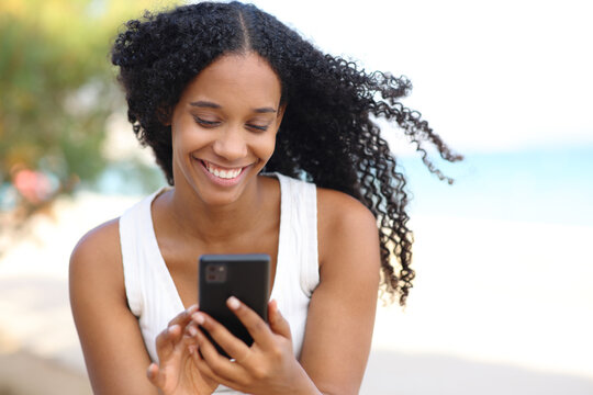 Happy black woman using phone on the beach