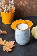 Pumpkin latte with fall leaves and pumpkin on dark background