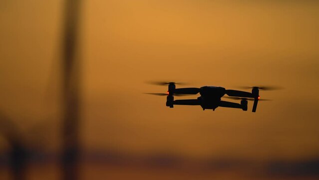 Drone inspecting wind turbines farm at breathtaking variegated cloudy sundown, quadrocopter uses for study advantages and drawbacks of electric station. Ecology Safe Alternative Energy Source
