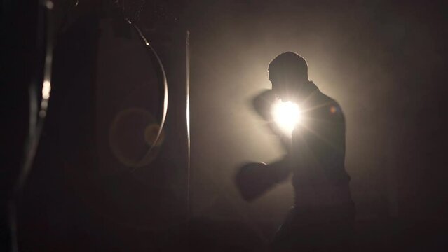 Strength, attack and motion concept. Boxer over dark gym background. Athlete in black gloves. Sporty young man during boxing