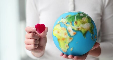 Woman holds toy heart and globe in hands showing love for planet and travelling. Support and respect for environment. Nature protection concept