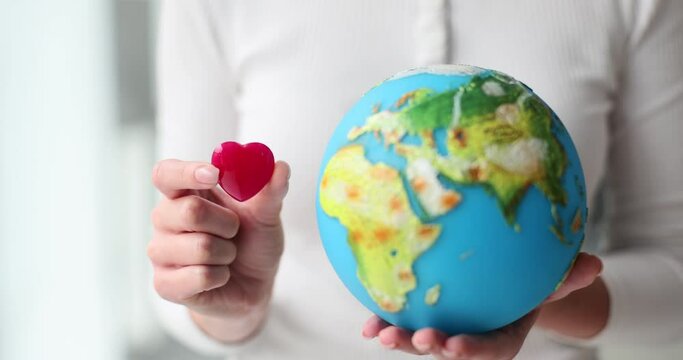 Woman holds toy heart and globe in hands showing love for planet and travelling. Support and respect for environment. Nature protection concept