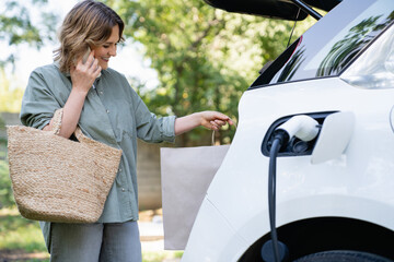Woman with shopping bag next to a charging electric car.