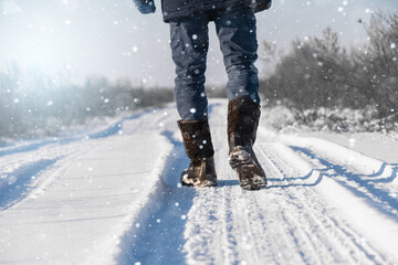 A traveler in boots walks along a snowy winter road - obrazy, fototapety, plakaty
