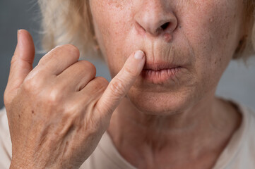 Naklejka premium Unhappy elderly woman pointing at wrinkles around her lips. 