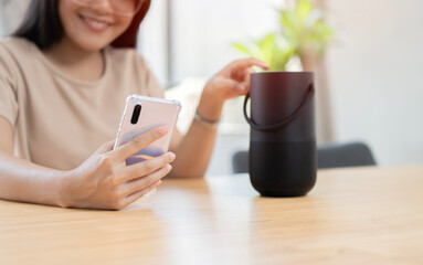 Modern trendy Asian girl listening to music by wireless portable speaker. Young beautiful woman enjoying at home.