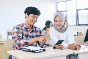 Happy college students looking at mobile phone together in classroom 