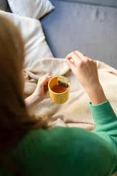 Woman dipping teabag in mug on sofa at home