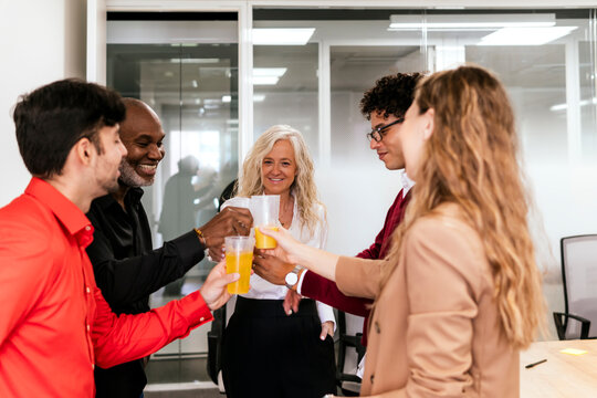 Multiracial businessmen and businesswomen toasting juice glasses in office