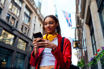 Smiling woman with eyeglasses and headphones using mobile phone in city