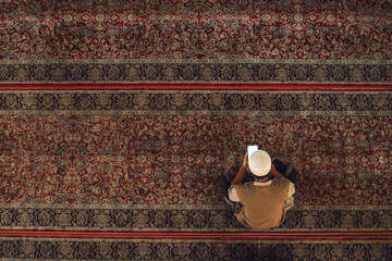 Top view of an unidentified Muslim man read Quran from mobile phone in a mosque