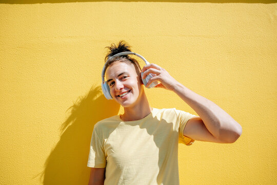 Smiling man wearing wireless headphones in front of yellow background