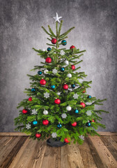 Ornamental Christmas tree on wooden floor with gray textured wall, with red, silver and teal baubles
