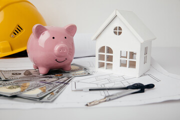 House building costs concept. Yellow helmet and piggy bank with blueprint