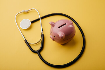 Stethoscope with piggy bank on a yellow background. Savings or medical insurance