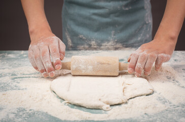 Baker rolls out dough for pizza, flatbread or pastry with rolling pin, prepare ingredients for...
