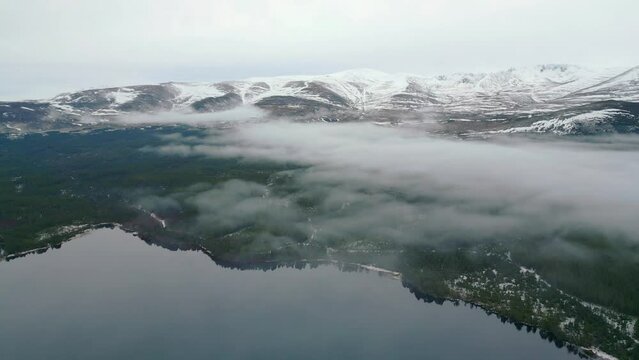 Flying through mist over a glass-like loch Ness towards snow-covered mountains 