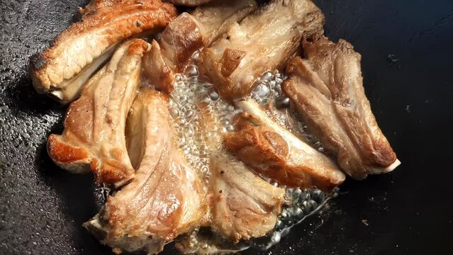 Pork ribs are fried in a cauldron in super slow motion. Meat with a golden crust. Cooking footage.