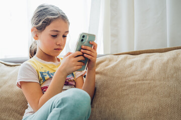 Cute little kid girl using digital tablet technology device lying on sofa alone. Small child hold...