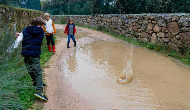 Children playing outside throwing stones into a large puddle