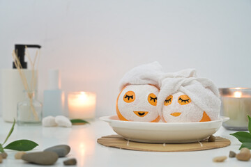 Oranges in face masks and towels surrounded by candles on white background. Spa treatment concept