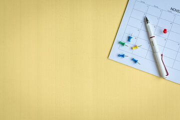 Calendar with colorful pins and pen, top view. Copy space.
