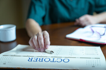 Close up view of woman reaching out to a pen on top of a calendar, next to notepad. Meeting or schedule planning concept.