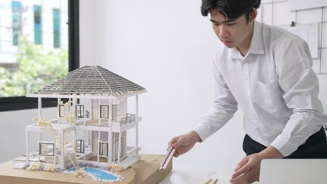Close up of professional male architect engineer measure house model and using laptop analysis data at meeting table with house model and map . scatter around. Focus on hand. Immaculate.