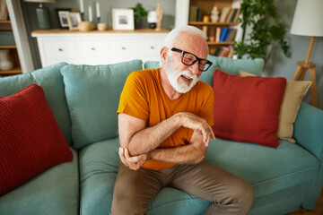 Unhappy senior man suffering from elbow pain at home
