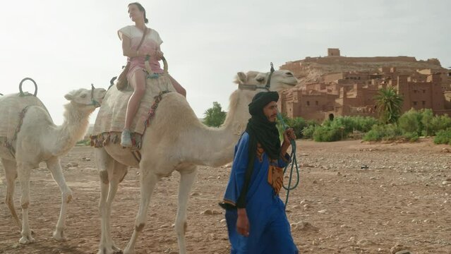 Woman riding a camel in front of Ait Benhaddou old town, Morocco