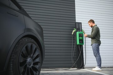 A man stands near a charging station and charges his electric car
