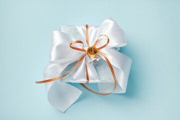 Gift box wrapped in blue silver paper with white and gold ribbon bow and bells. Blue background,...