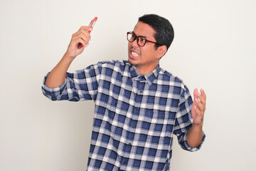 Naklejka premium Adult Asian man showing angry expression when holding his mobile phone