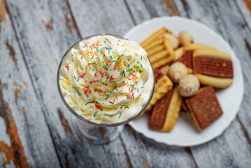 Milkshake with whipped cream decorated with sprinkles on a wooden table. Milkshake and sweet cookies.