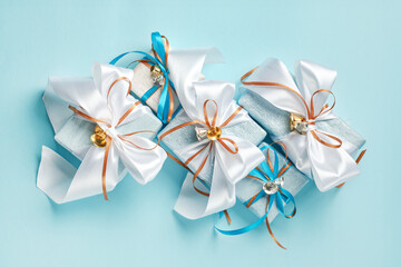 Gift boxes wrapped in blue, white and silver paper with white, blue and gold ribbon bows and bells. Blue background, top view. Christmas and New Year gifts, Boxing Day.