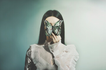 woman holds a butterfly in front of her face; abstract concept