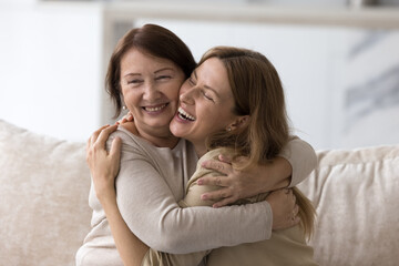 Happy loving elder mom embracing beautiful adult daughter woman with joy, tenderness, smiling, laughing at joke together, giving comfort, support, care, enjoying being parent, motherhood - obrazy, fototapety, plakaty