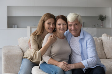 Happy senior woman enjoying warm good relationship with adult daughter and loving older husband, posing with family for shooting, looking away, smiling, laughing