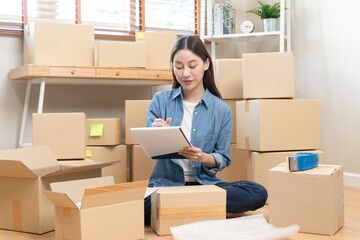 Young Asian woman owner of small online store packing customer orders in the home office.