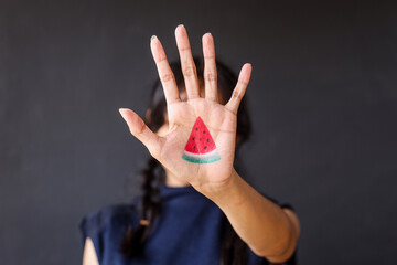 Woman showing hand painted with slice of watermelon to the camera. Symbol of support for Palestine - obrazy, fototapety, plakaty