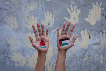 Hands painted with Palestinian flag and watermelon slices against hand prints on the wall in the background. Stop war, peace and humanity concept - obrazy, fototapety, plakaty